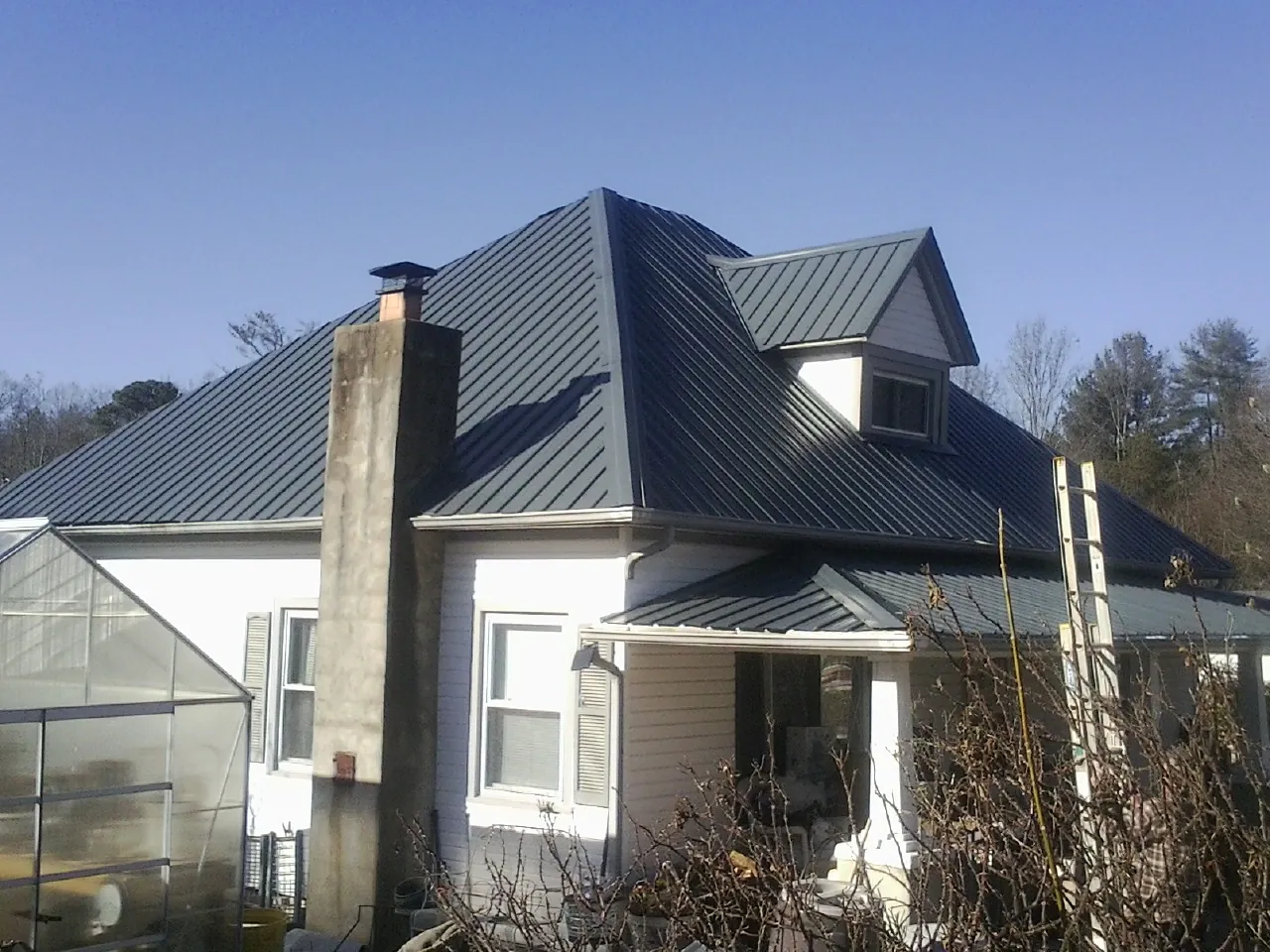 Dark blue standing seam metal roof on a white farmhouse with dormer — Slate & Tile Roof Repair by Roofing Brothers in Patterson