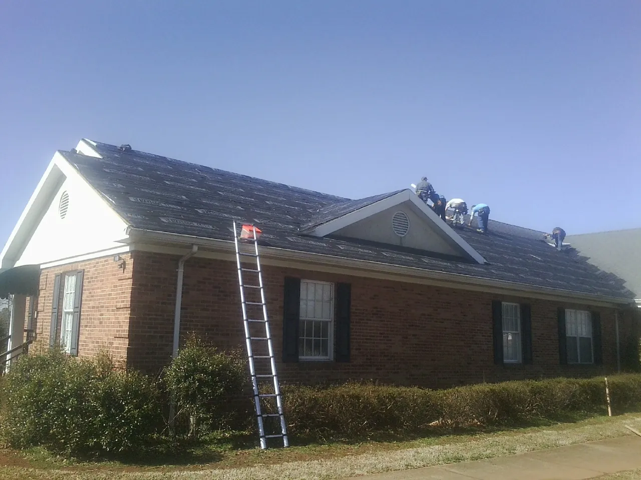 Crew tearing shingles off a brick ranch roof with a ladder set — Emergency Roof Repair work by our crew in Patterson