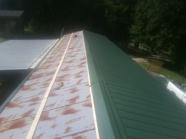 Old rusted panels beside newly installed green metal roofing — Wind Damage Roof Repair by Roofing Brothers in Patterson