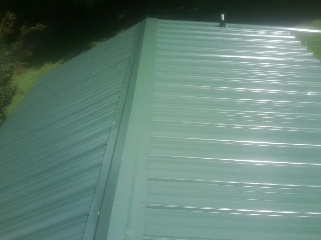 New green metal panels meeting at the ridge of a roof — Flat Roof Repair work by our crew in Patterson