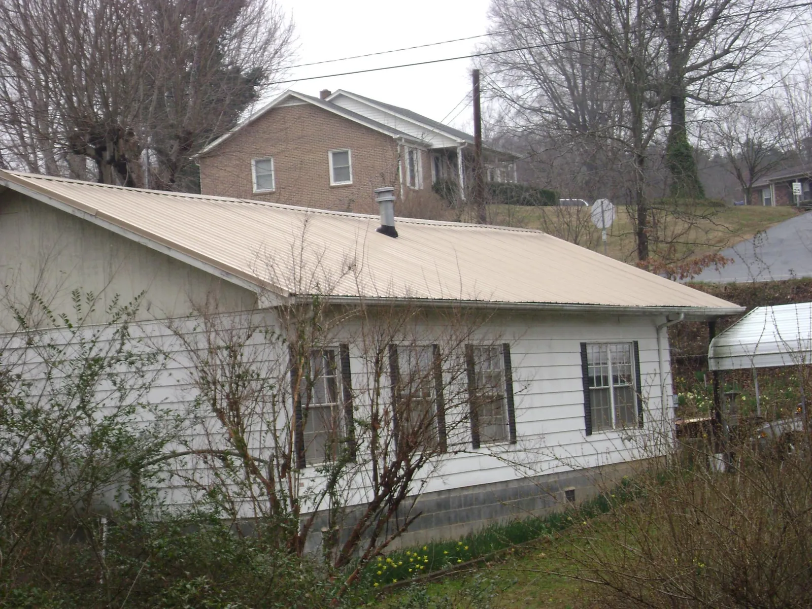 Tan metal roof on a white sided house set into a hillside — Commercial Roofing by Roofing Brothers in Patterson