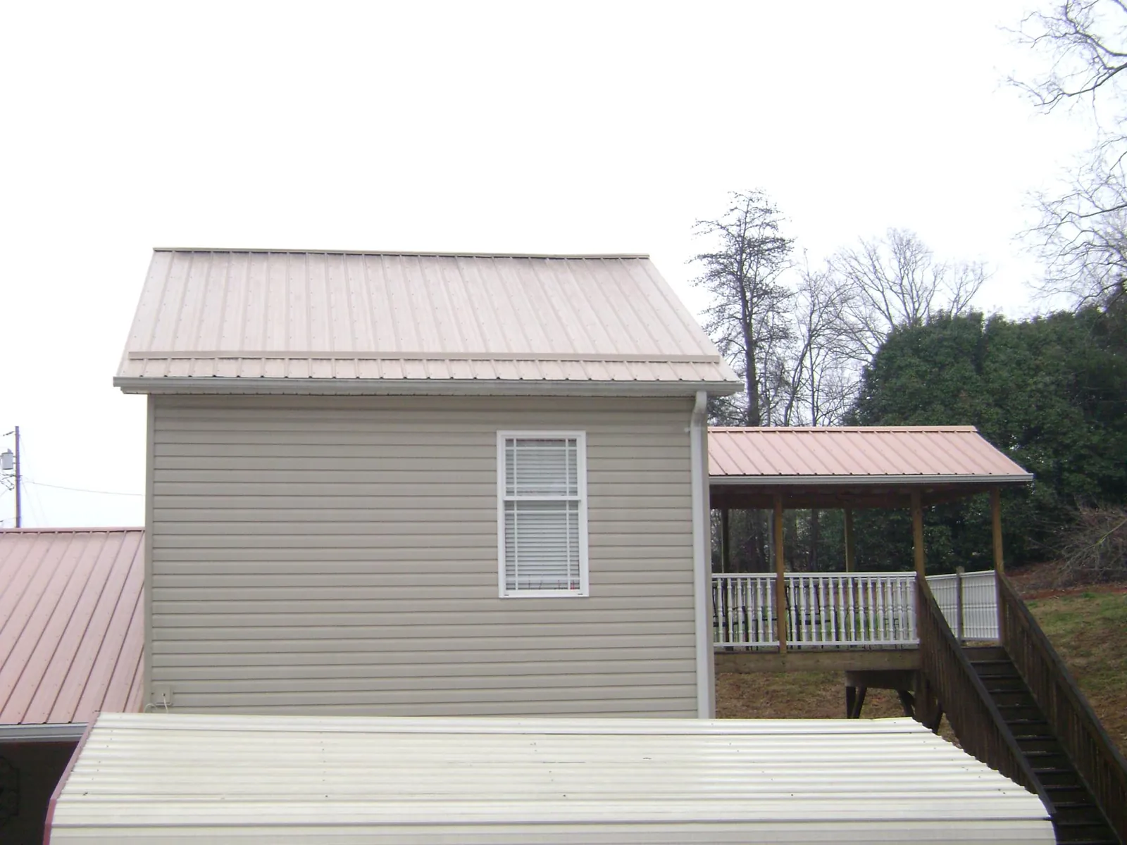 Tan metal roofs on a two story addition and attached porch, from a Roof Replacement job in Patterson